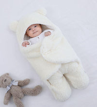 Baby wrapped in a cozy white quilted sleeping bag with bear ears, beside a plush teddy bear.